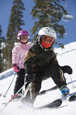 children skiing downhill with helmets and goggles